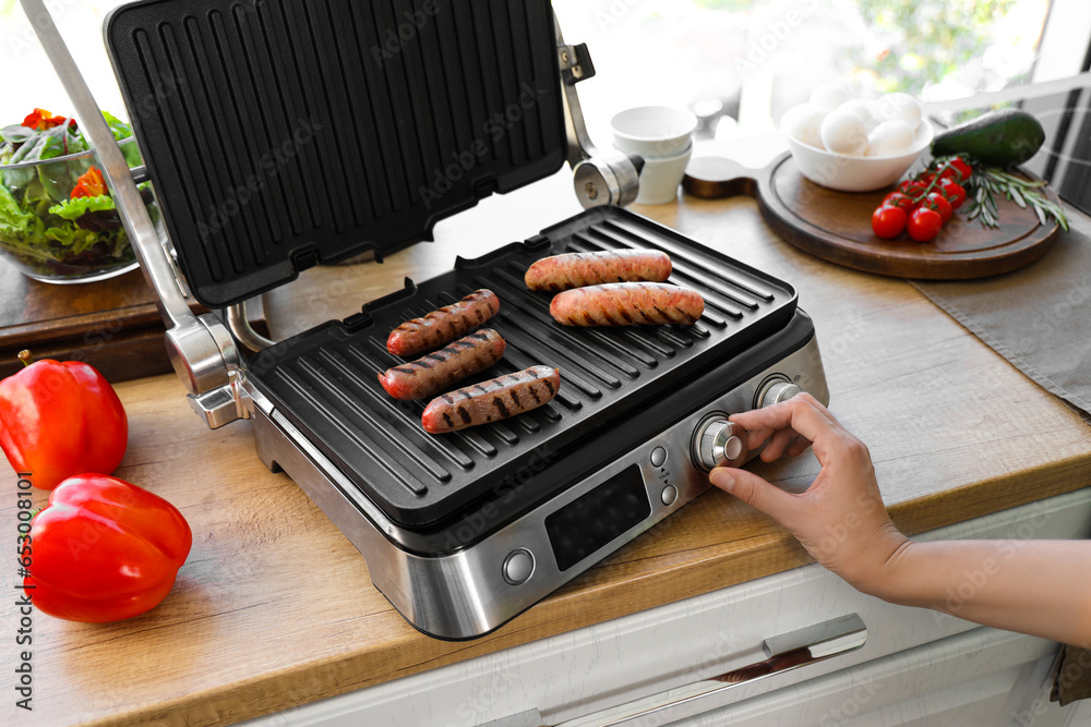 Woman cooking delicious sausages on modern electric grill in kitchen, closeup