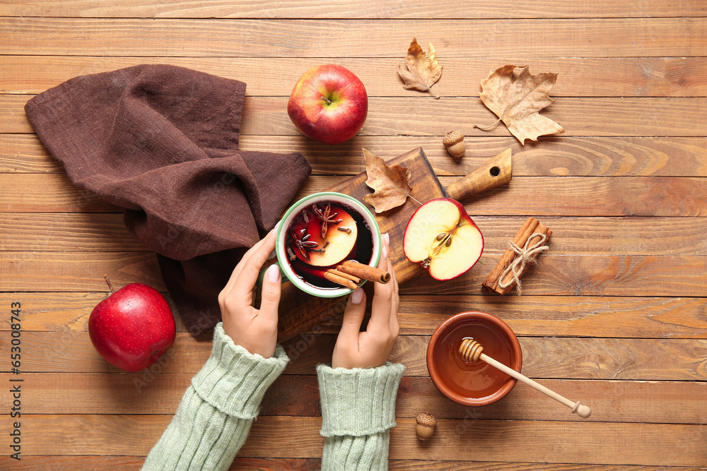 Female hands with cup of hot mulled wine and apple on wooden background