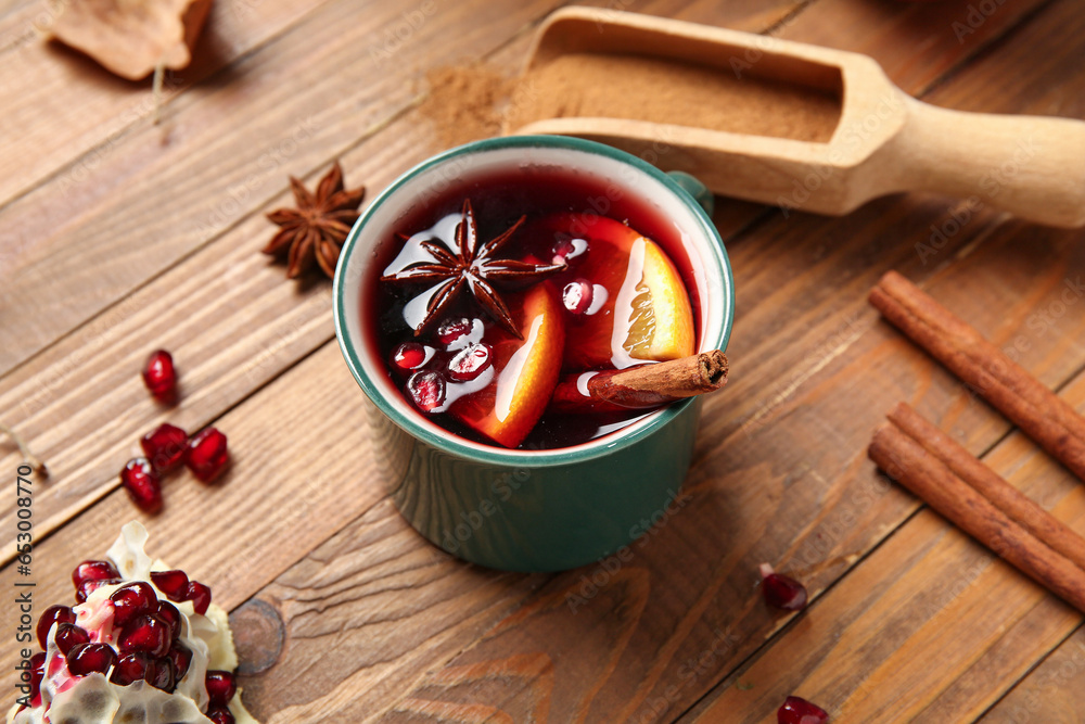 Cup of hot mulled wine with orange and pomegranate on wooden background