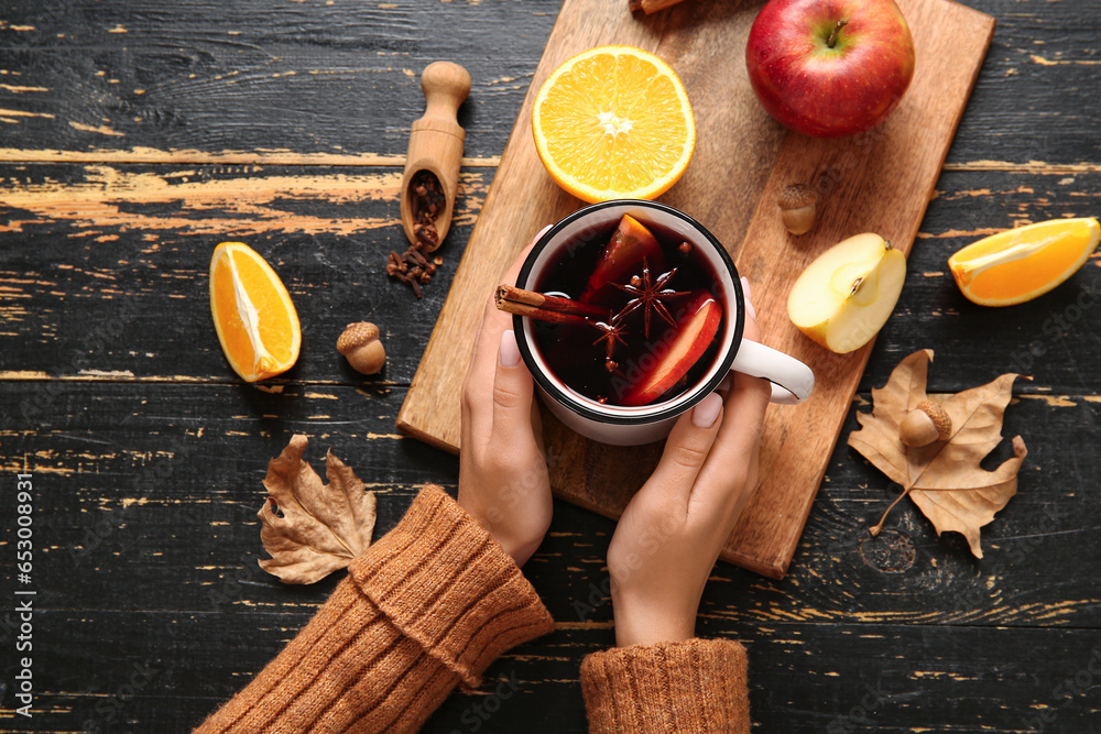 Woman holding cup of hot mulled wine with apple and orange on black wooden background