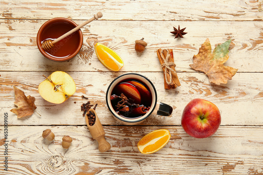 Cup of hot mulled wine with apple and orange on white wooden background