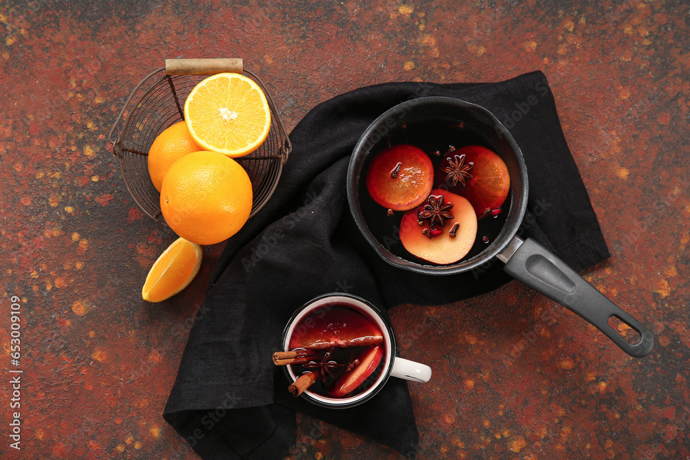 Saucepan and cup of hot mulled wine with orange on dark background