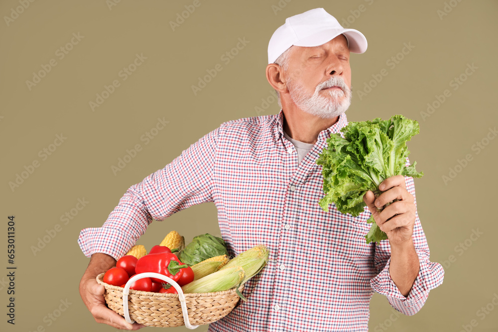 Mature male farmer with wicker basket full of different ripe vegetables on green background