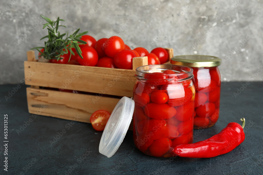 Jars of pickled tomatoes with chili pepper and rosemary on dark table