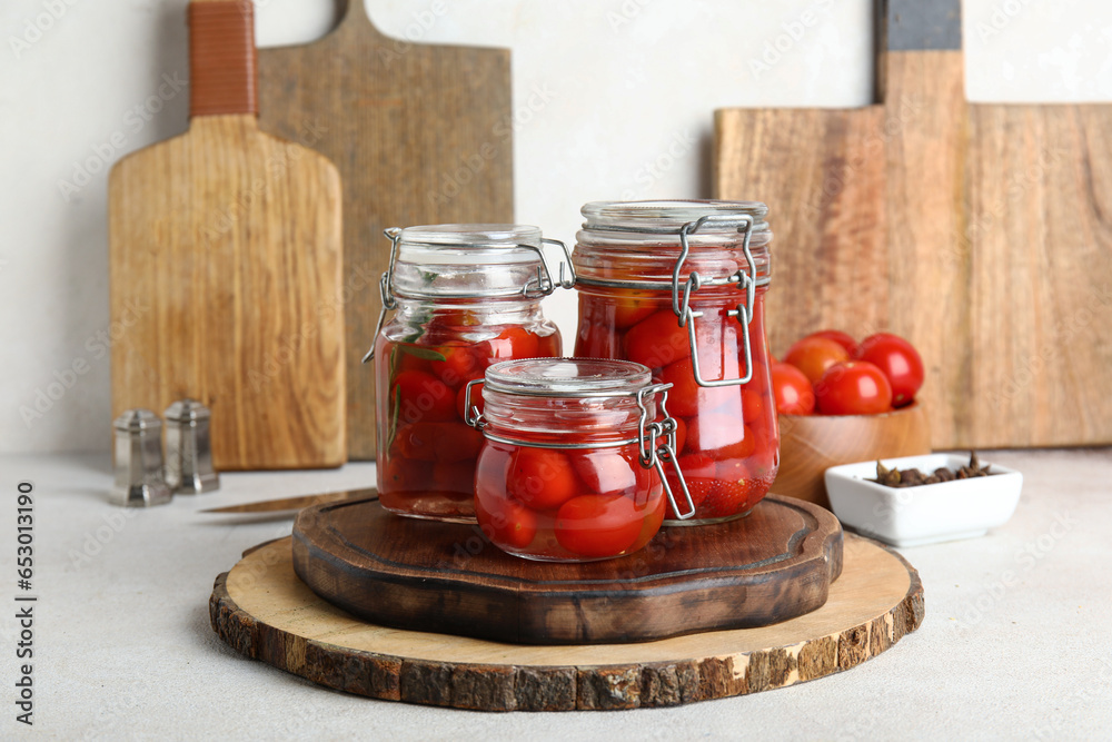 Wooden board with jars of pickled tomatoes on white background