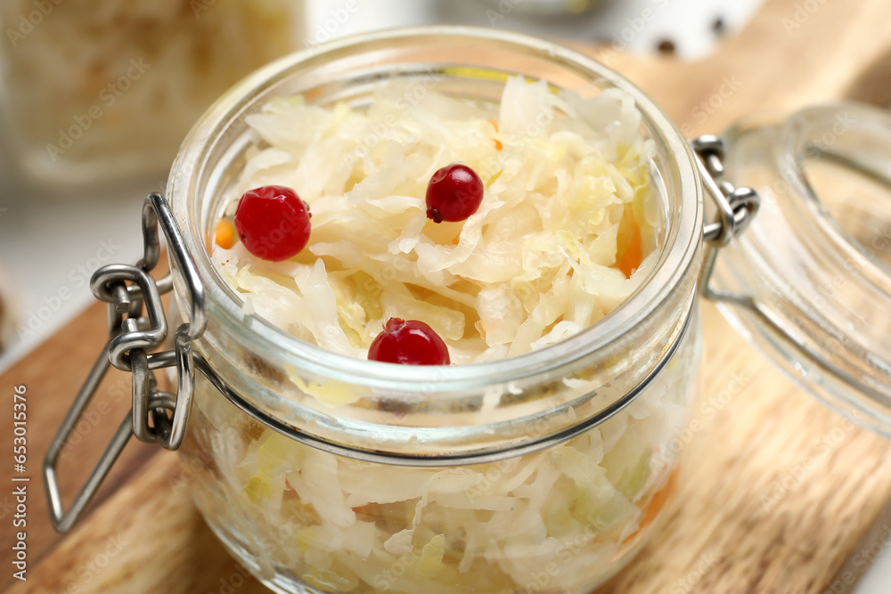 Wooden board with jar of delicious sauerkraut and viburnum on white background, closeup