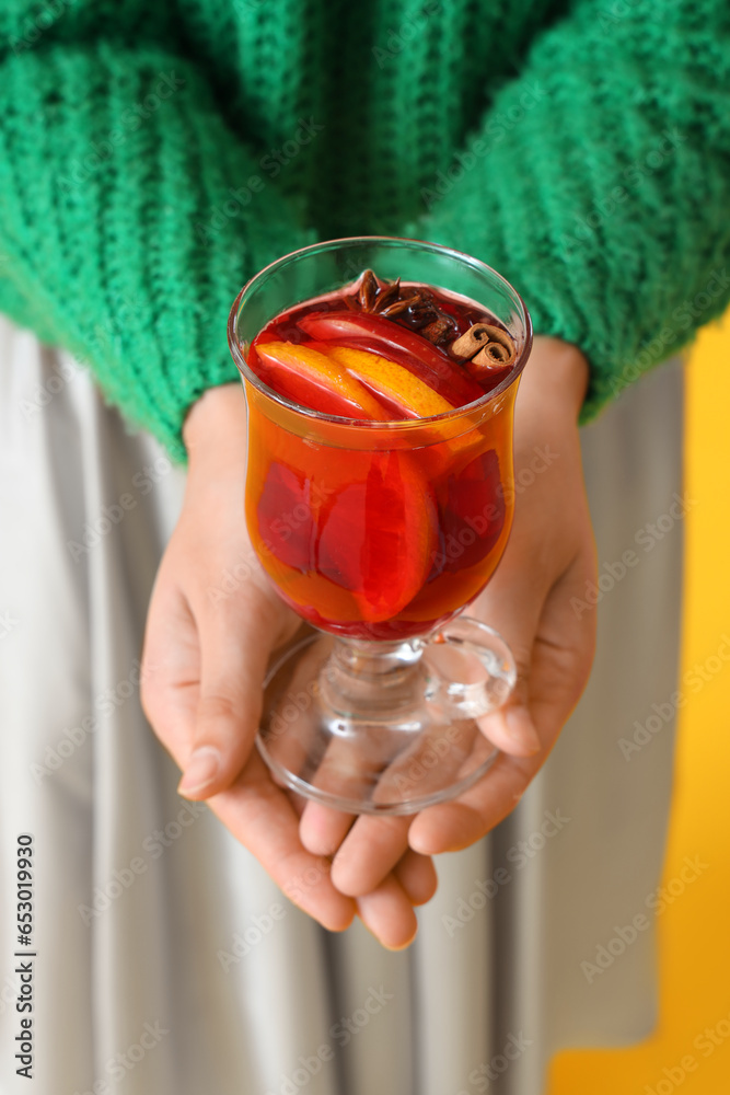 Young woman with glass of mulled wine on yellow background, closeup