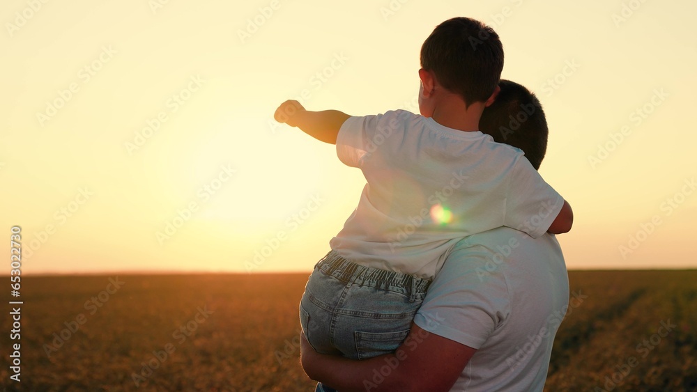 Father and child stretch their hand to sun, kid plays with dad. Dad, son in field watching sunset. Concept of happy family, unity with nature. Walk son, dad outdoor. Child is in arms of father, family