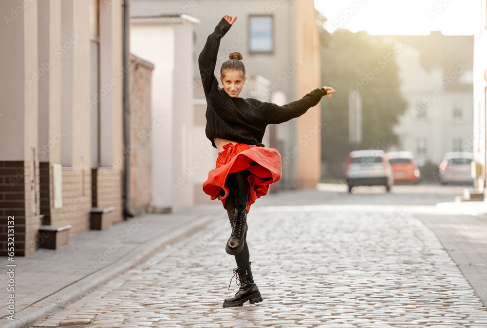 Beautiful teenager girl in red skirt dancing at city street with daylight. Pretty teen model in trendy clothes performing in old town portrait