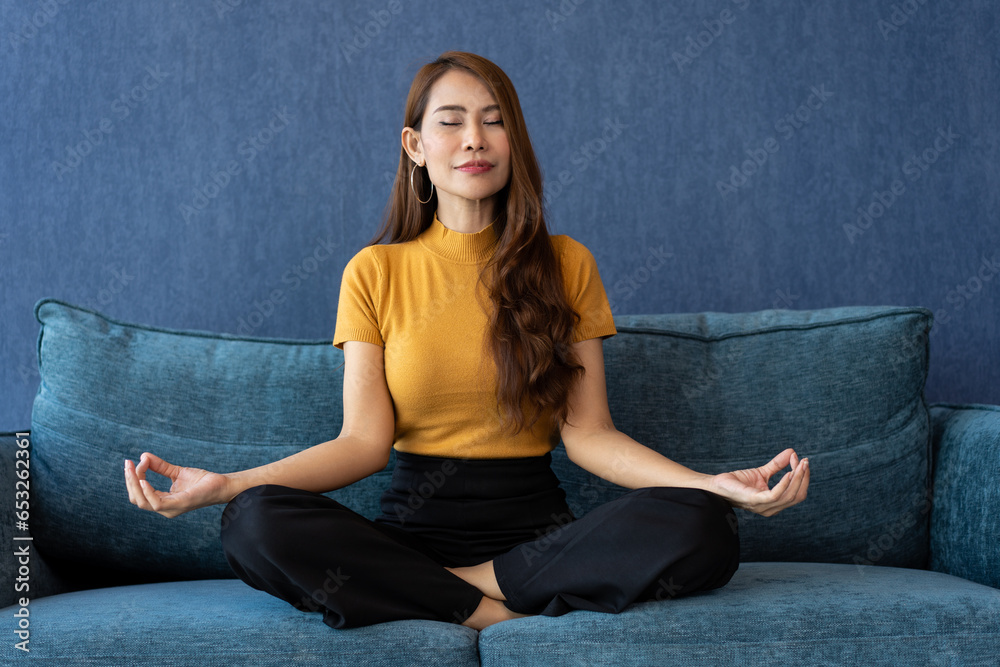 Portrait of healthy Asian woman meditating and exercise pose yoga on the sofa in morning. Zen relaxation and mindfulness lifestyle, Concept of indoor workout for good healthy and breathing practice.