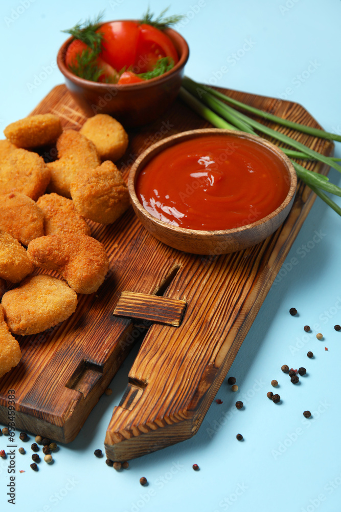 Wooden board with tasty nuggets and ketchup on blue background