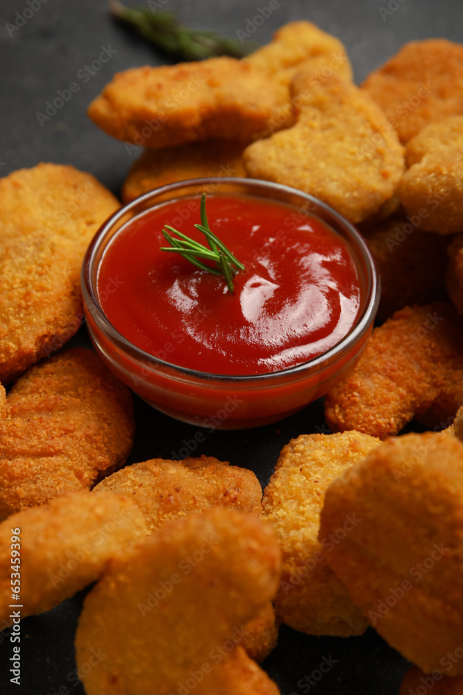 Bowl with ketchup and tasty nuggets on dark background, closeup