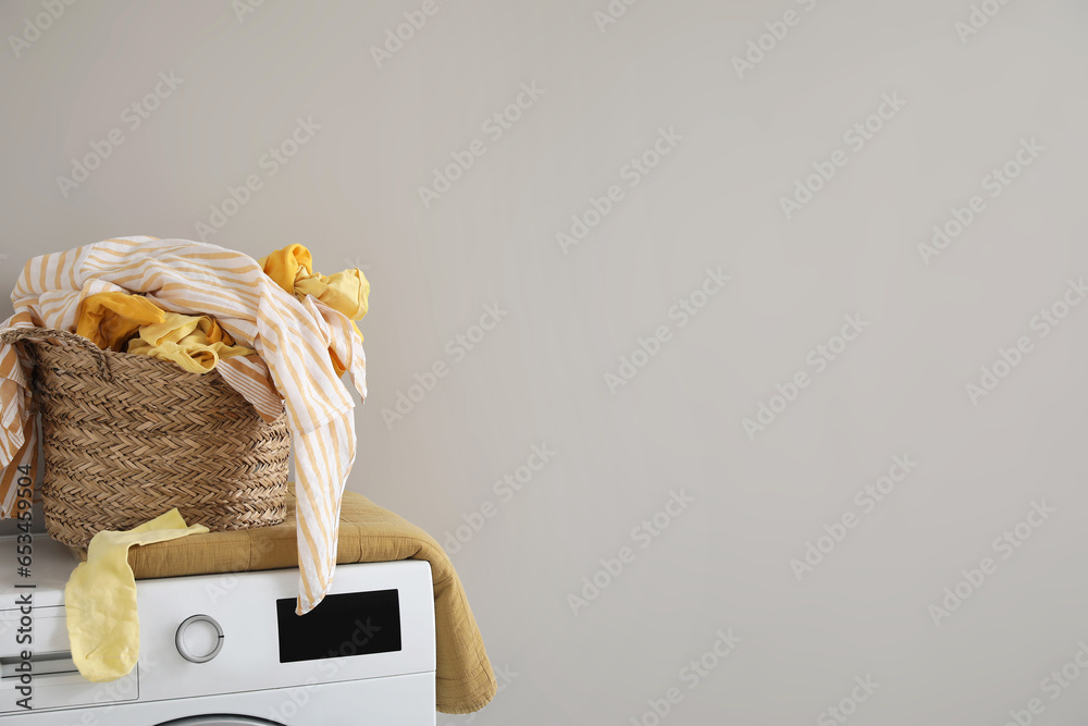 Laundry basket with dirty clothes on washing machine near light wall, closeup