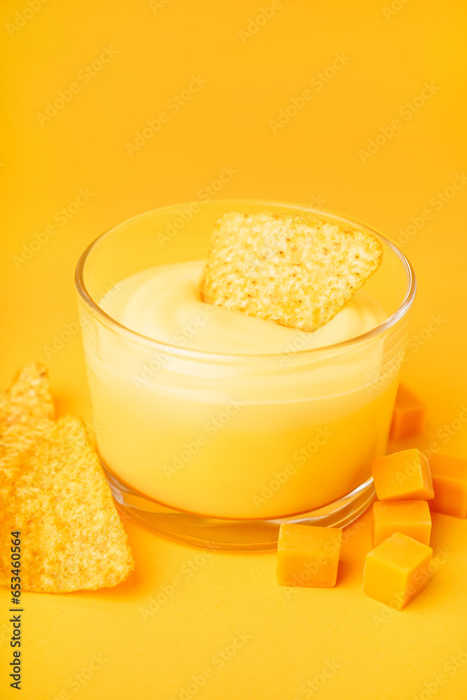 Bowl with tasty cheddar cheese sauce and nachos on yellow background