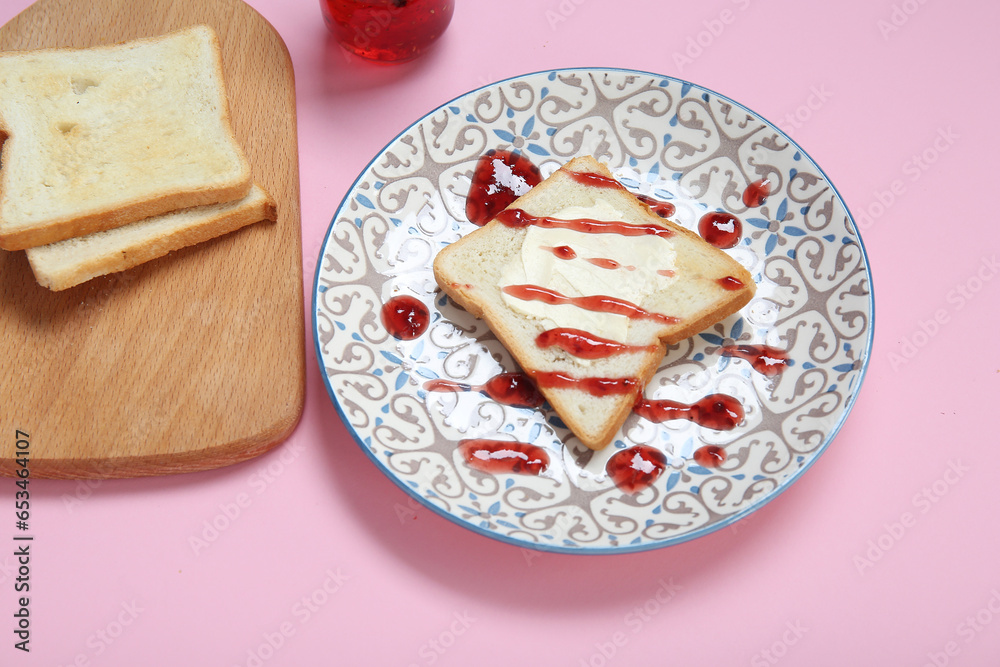 Plate of toast with butter and jam on pink background