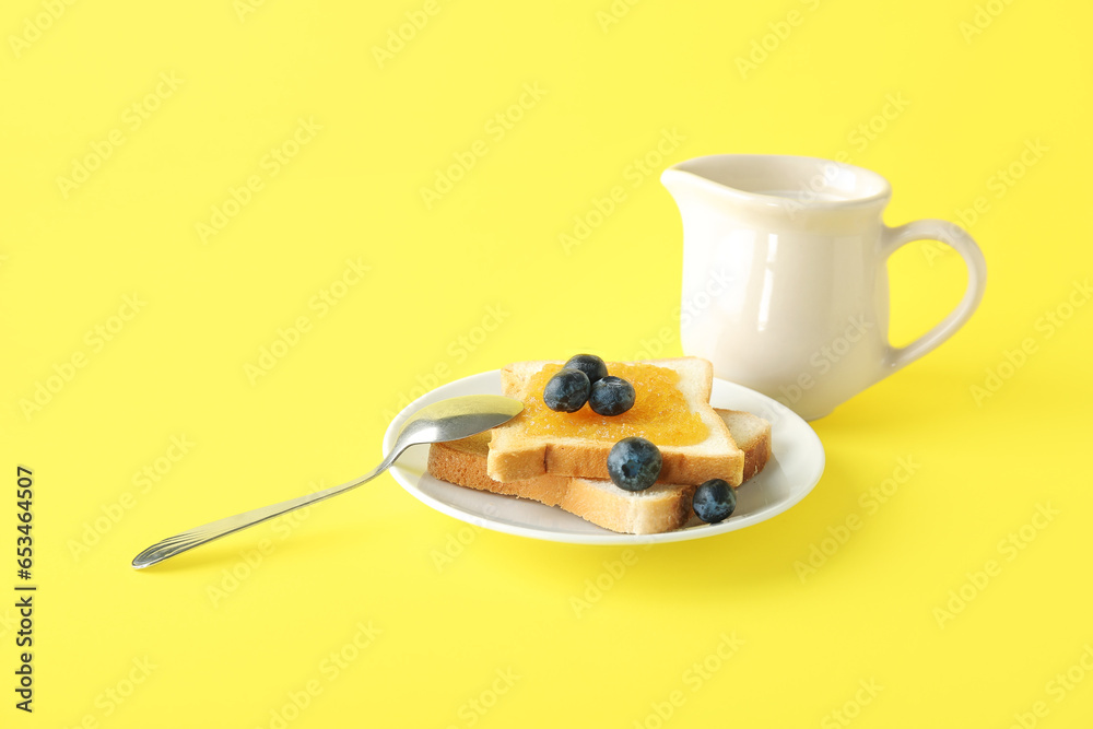 Plate of tasty toasts with peach jam, blueberry and milk in pitcher on yellow background