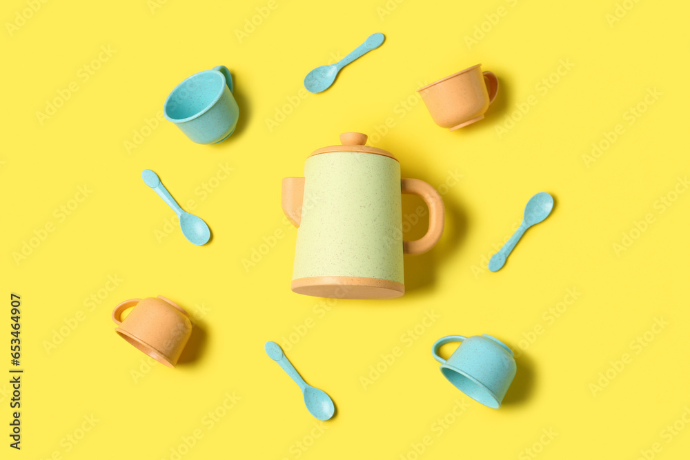 Teapot with frame made of different cups and spoons for baby on yellow background