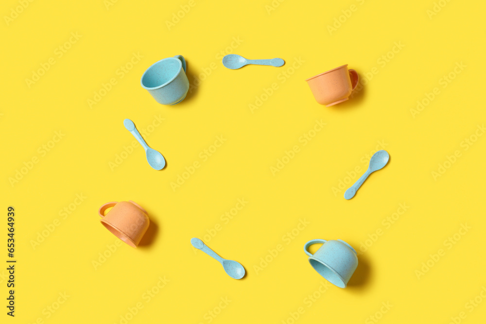 Frame made of different cups and spoons for baby on yellow background