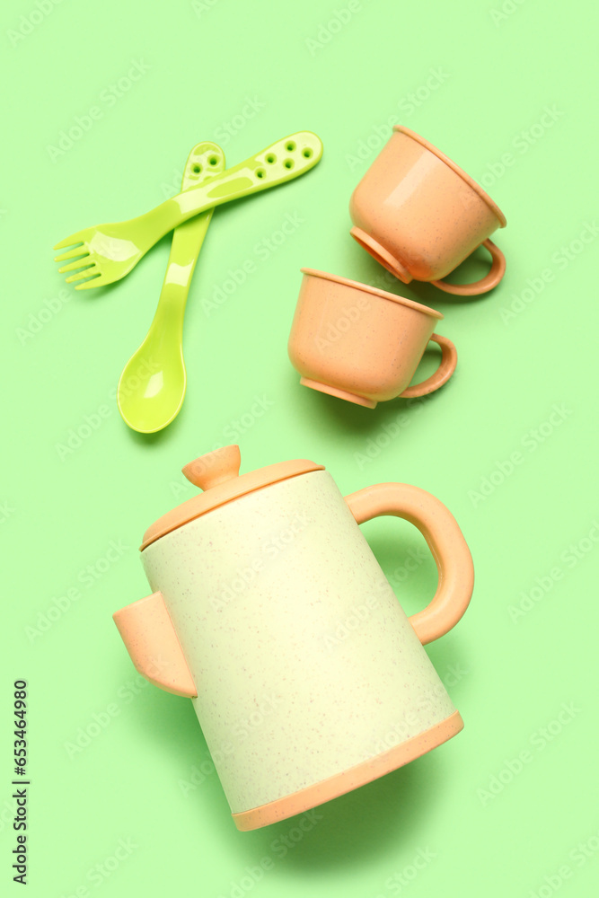 Teapot with cups and cutlery for baby on green background