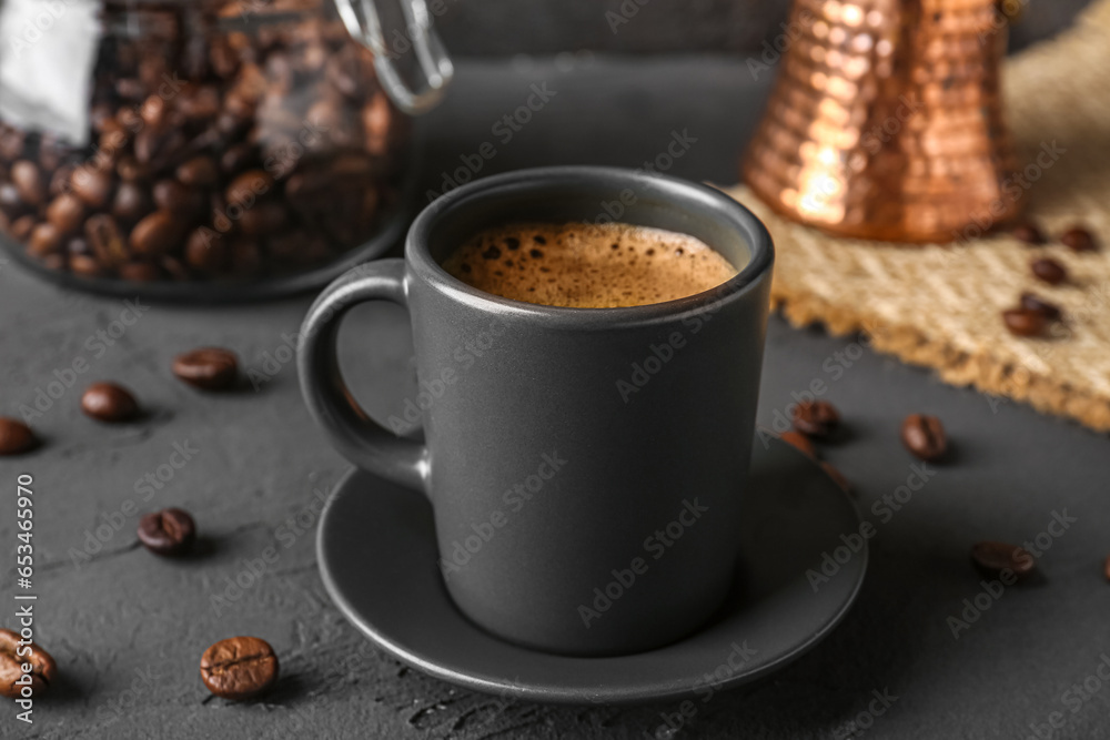 Cup of delicious espresso with coffee beans and saucer on grey background, closeup