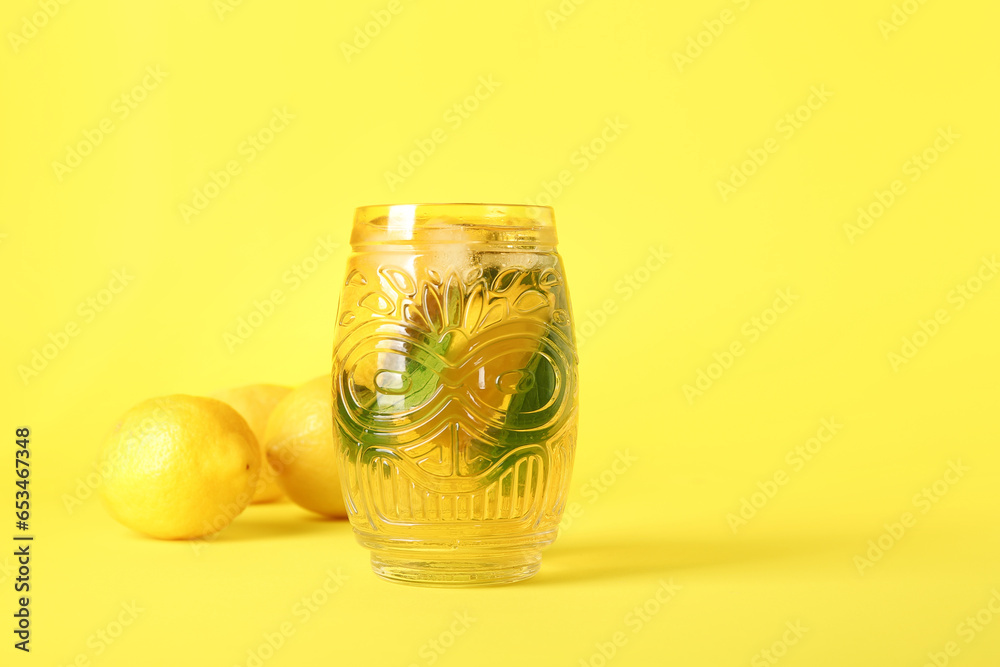 Glass of ice tea with lemon and mint on yellow background