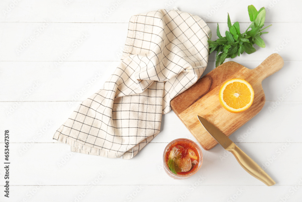 Glass of ice tea and board with orange on white wooden background