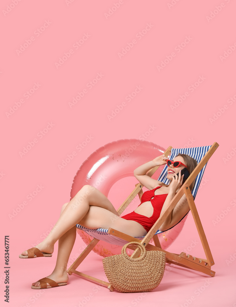 Young woman with beach accessories talking by mobile phone on pink background