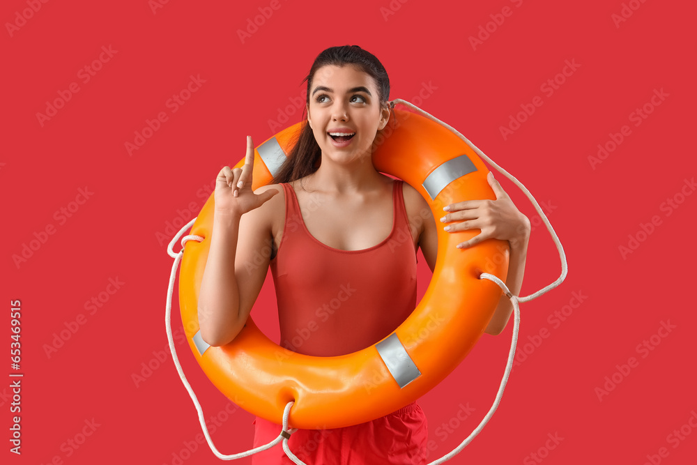 Female lifeguard with ring buoy pointing at something on red background