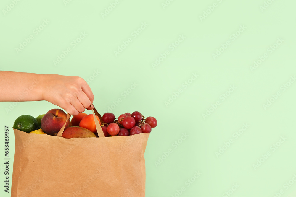 Female hand with paper bag full of fresh fruits on green background