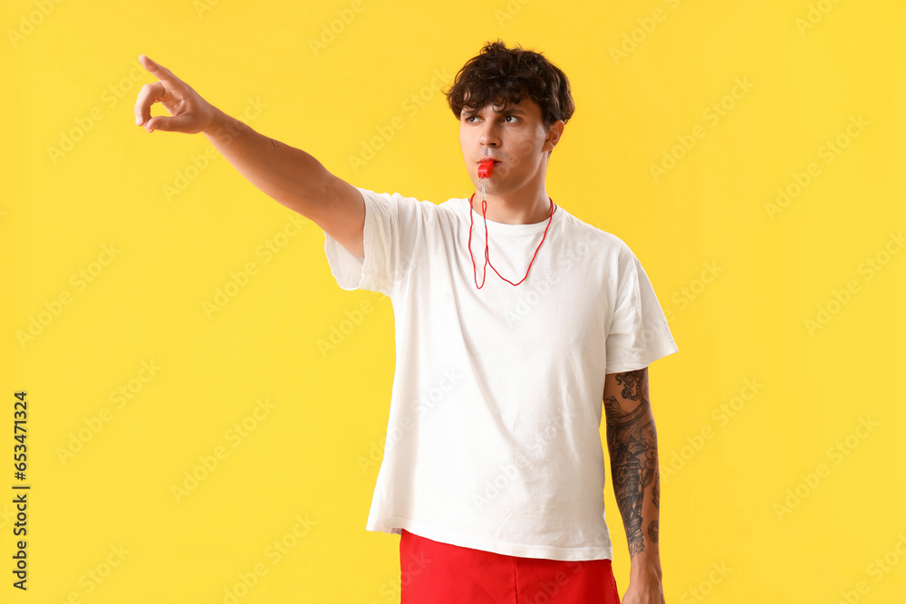 Male lifeguard with whistle pointing at something on yellow background