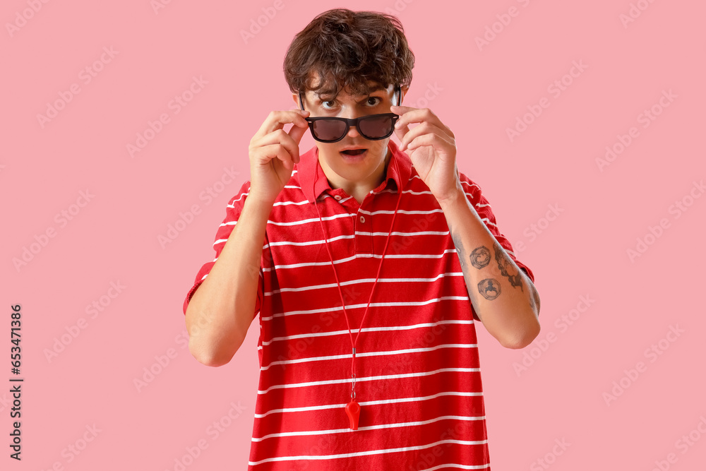 Shocked male lifeguard in sunglasses on pink background