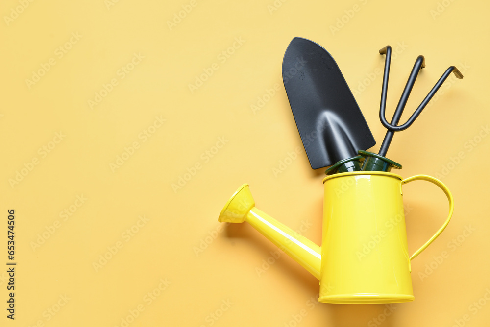 Watering can with gardening rake and shovel on yellow background