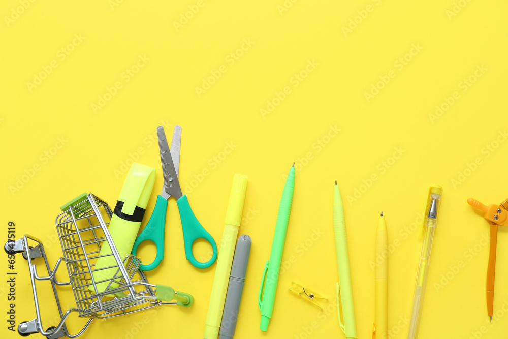 Shopping cart with different stationery on yellow background