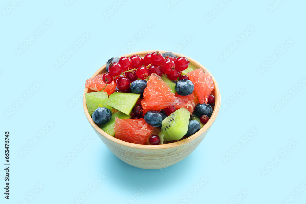 Bowl with fresh fruit salad on blue background