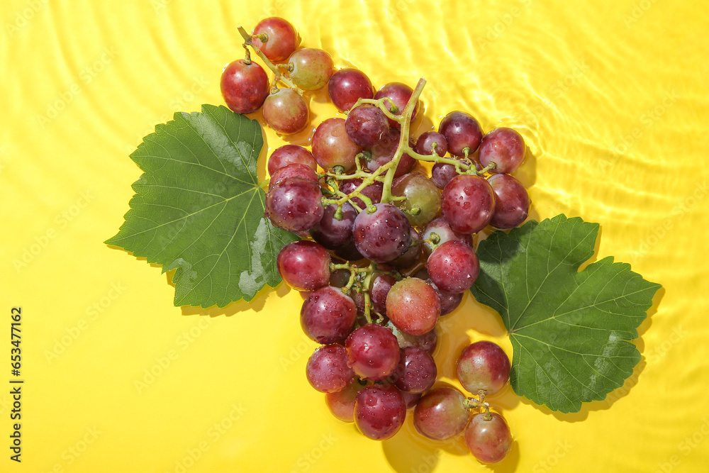 Tasty ripe grapes with leaves in water on yellow background