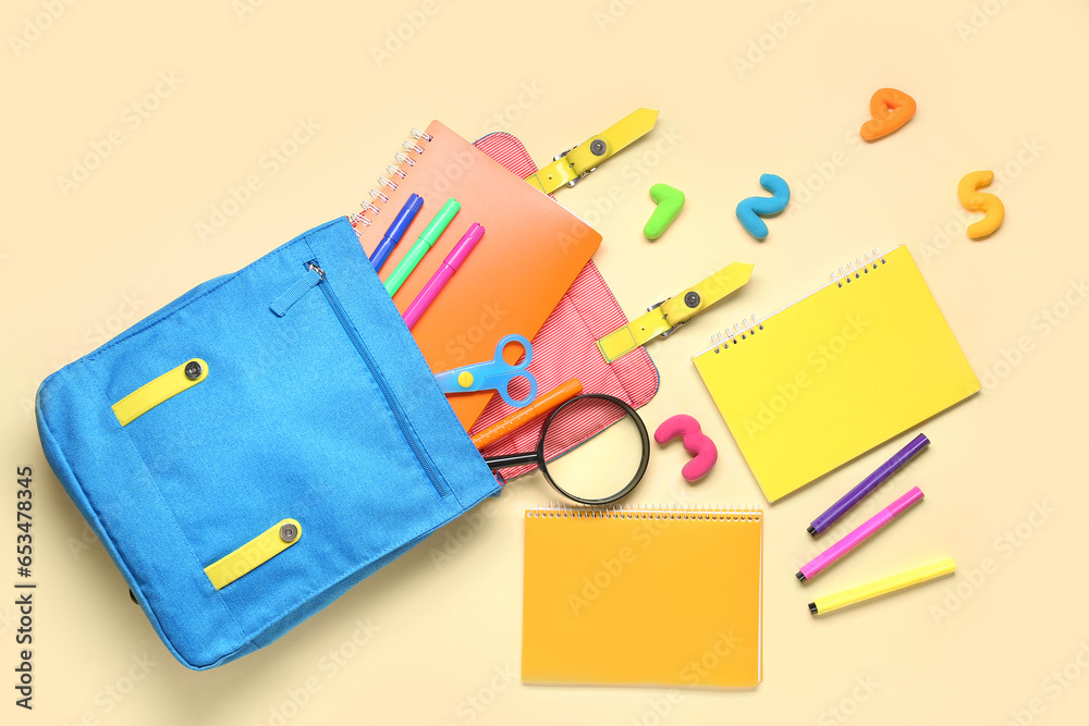 School backpack with different stationery on pale yellow background