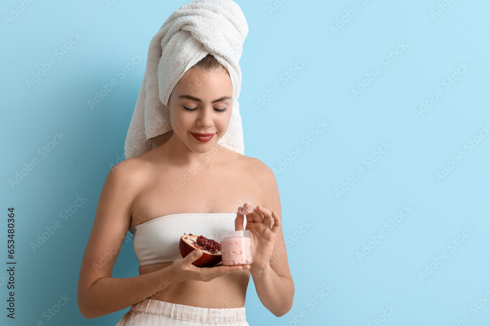 Young woman with pomegranate and jar of cream on blue background