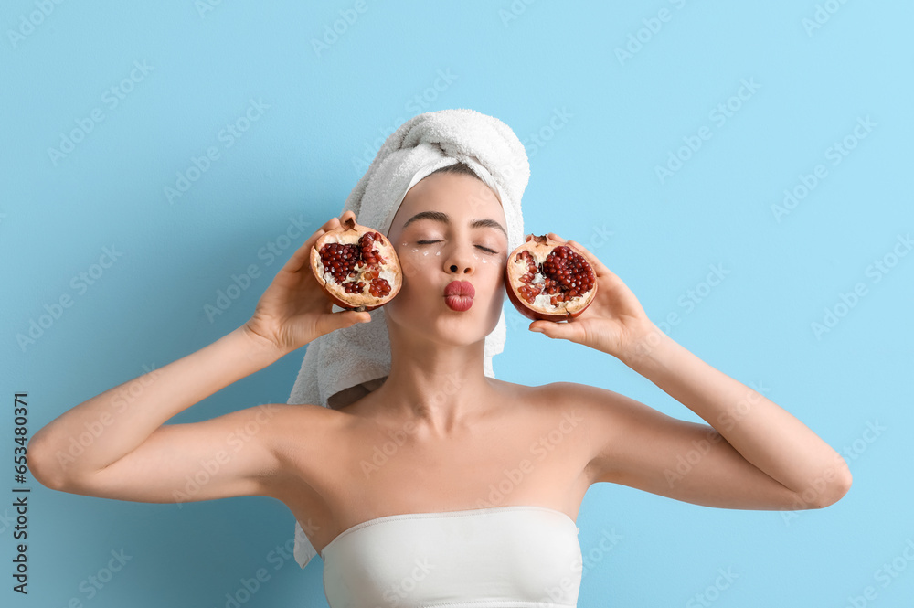 Young woman with pomegranate and under-eye cream blowing kiss on blue background