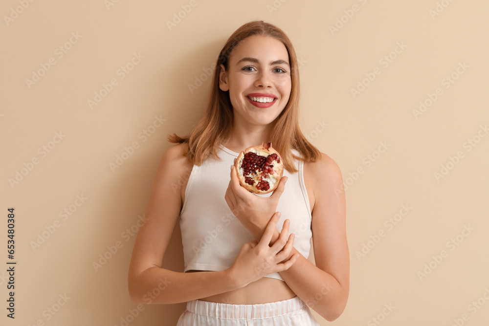 Young woman with pomegranate on beige background