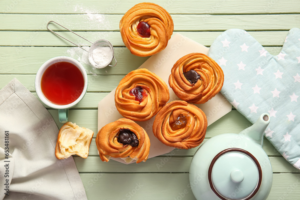 Board of tasty cruffins and cup of tea on green wooden background