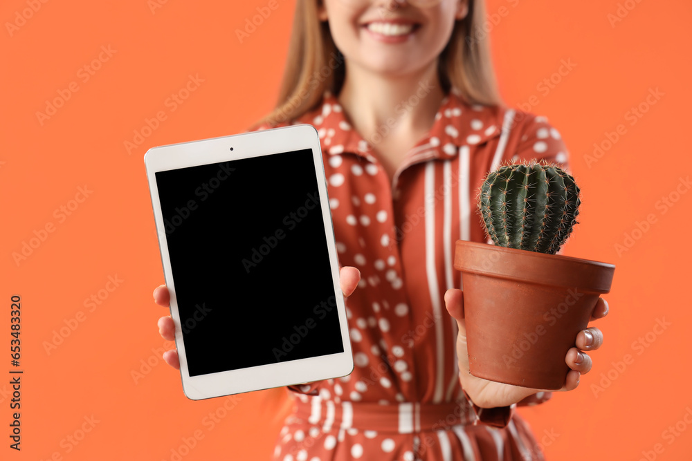 Young woman with tablet computer and cactus on orange background, closeup