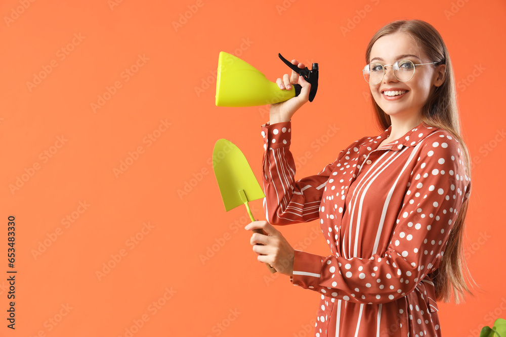 Young woman with shovel and spray bottle on orange background