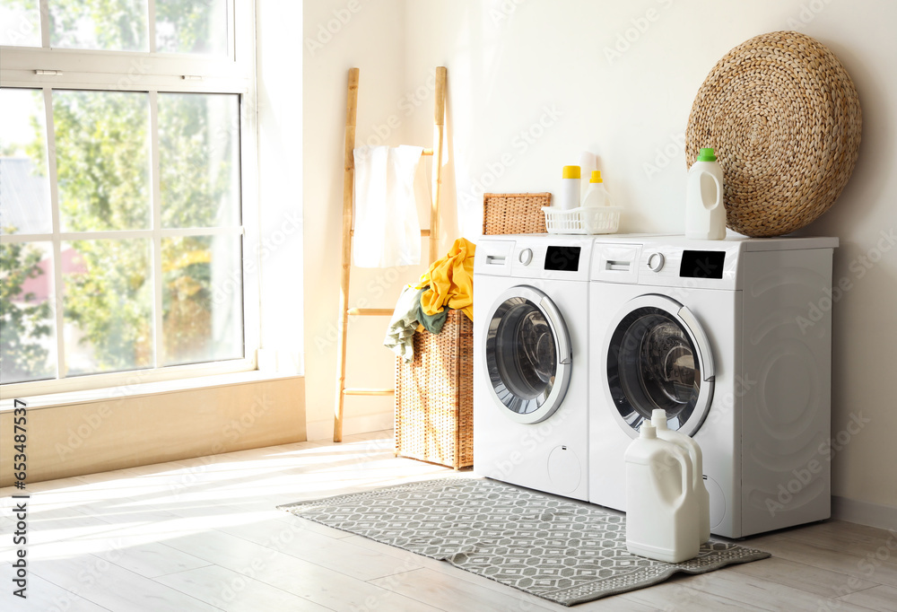 Interior of laundry room with washing machines and dirty clothes in basket