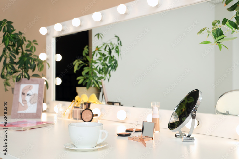 Dressing table with cosmetics and glowing mirror in makeup room, closeup