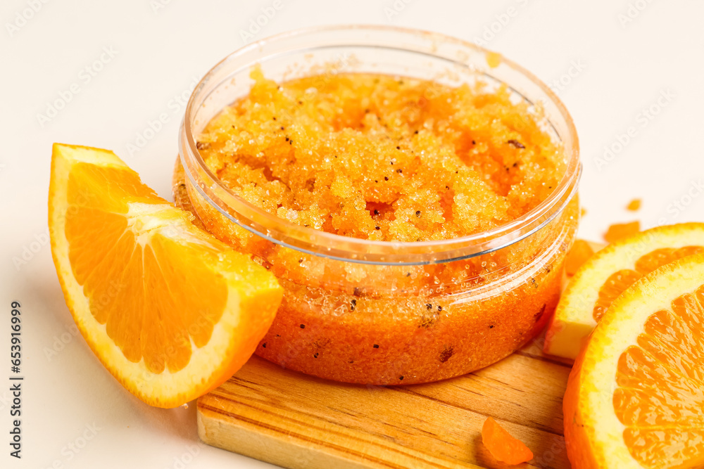 Wooden board with jar of natural body scrub and orange slices on light background, closeup