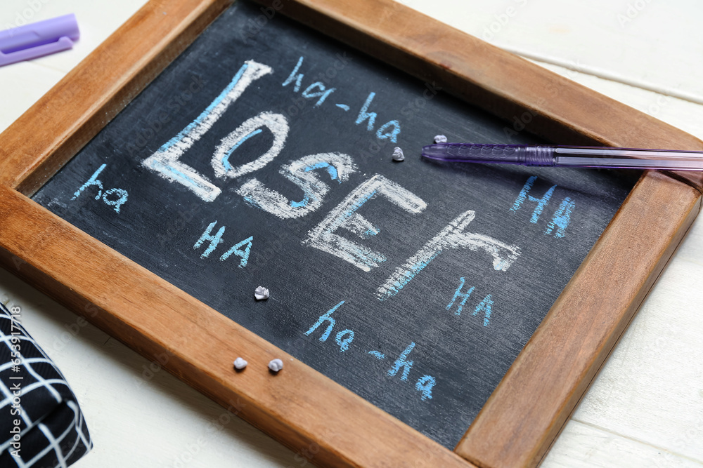 Chalkboard with word LOSER and school stationery on white wooden background, closeup