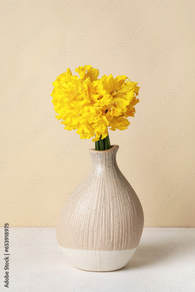 Vase with narcissus flowers on table near beige wall