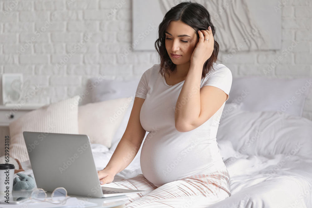 Young pregnant woman working with laptop in bedroom