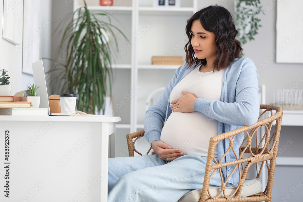 Young pregnant woman working at table in office