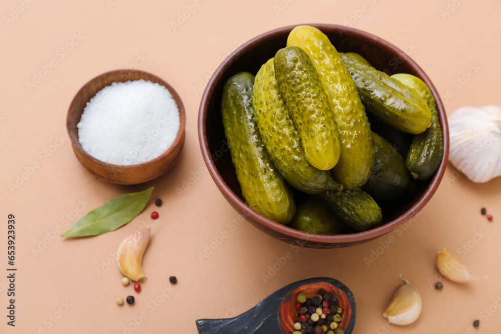 Bowl of tasty canned cucumbers with ingredients on beige background